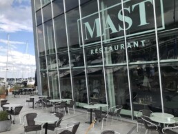 Udendørs siddepladser ved MAST Restaurant med borde og stole med udsigt over en marina